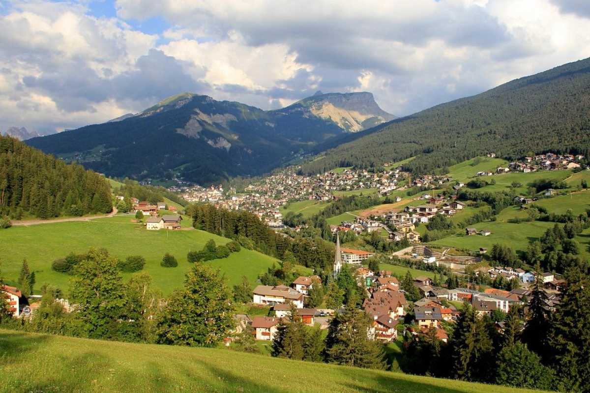 Famiglia con bambini che cammina tra i prati fioriti dell'Alpe di Siusi, sfondo con baite tipiche e montagne, atmosfera estiva e gioiosa