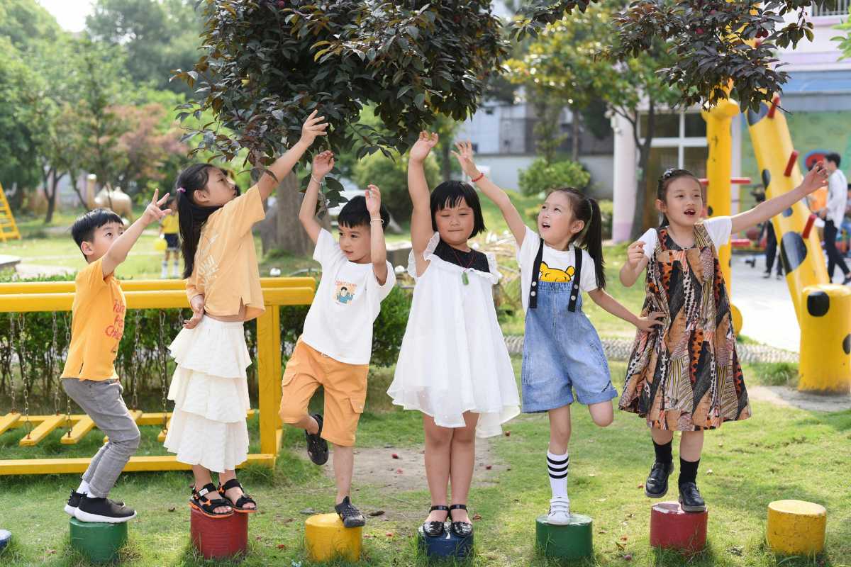 Bambini che giocano in un grande parco giochi di Ortisei, scivoli colorati, prato verde e montagne sullo sfondo, giornata di sole
