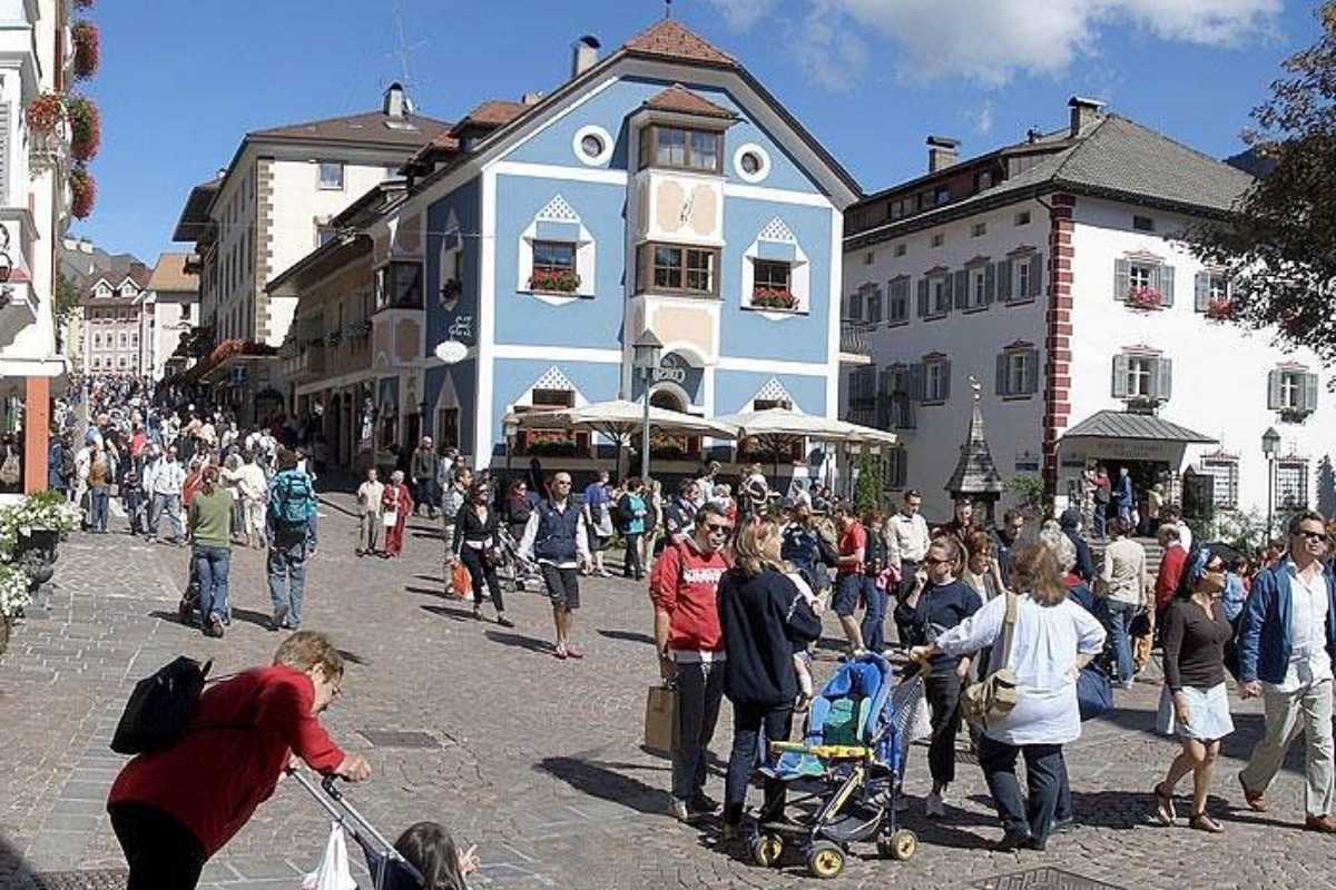 Vista panoramica di Ortisei, con scorcio delle case colorate del centro, il campanile e le Dolomiti sullo sfondo, atmosfera vivace di una giornata estiva